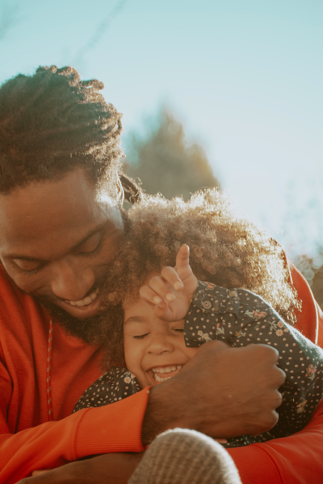 Pai abraçando filha sorrindo ao sol — futuro protegido com Previdência Infantil